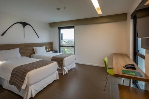 Quarto de hotel com duas camas de solteiro, escrivaninha, janela e decoração minimalista moderna.
