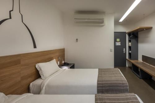 Quarto de hotel minimalista com uma cama de solteiro, cabeceira de madeira, decoração de parede, escrivaninha e ar-condicionado.