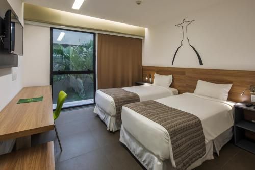 Quarto de hotel moderno com duas camas de solteiro, escrivaninha, TV e porta de varanda com vista para a área verde.
