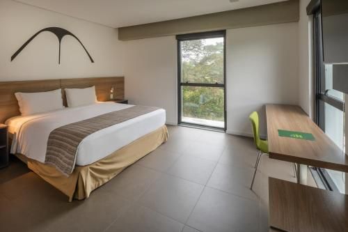 Quarto moderno com cama king-size, janela ampla, escrivaninha e móveis de madeira clara.