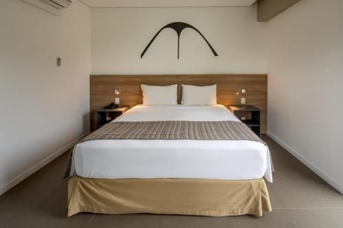 Quarto minimalista com cama centralizada, paredes brancas, cabeceira de madeira e arte na parede acima.