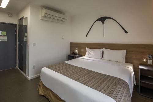 Quarto de hotel moderno com cama bem arrumada, cabeceira de madeira e ar-condicionado de parede.