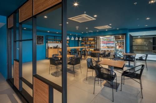 Café moderno com paredes azuis, janelas de vidro, mesas e cadeiras, e um balcão iluminado.