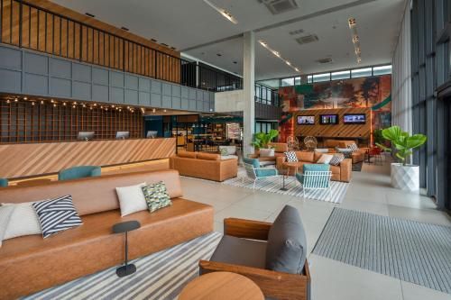 Lobby de hotel moderno com sofás em tons de bege, detalhes em madeira, tapetes listrados e poltronas sob tetos altos.