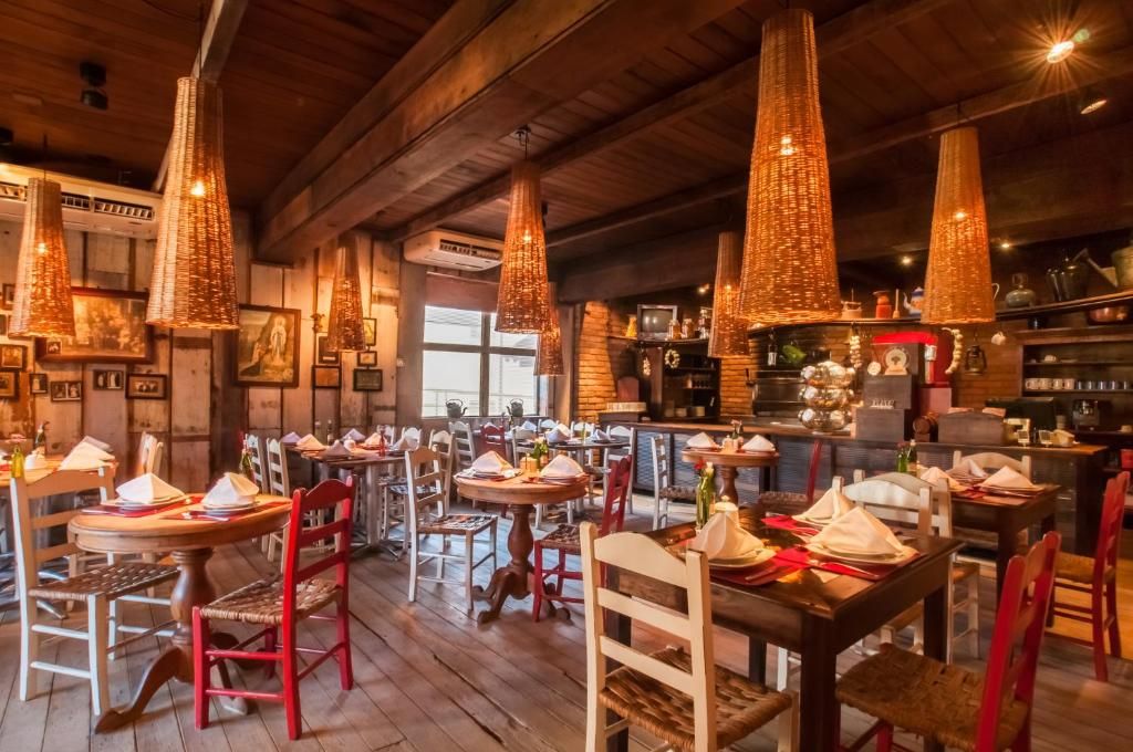 Interior aconchegante de restaurante rústico com mesas de madeira, cadeiras vermelhas, luminárias pendentes em tons quentes e mesas de jantar postas.