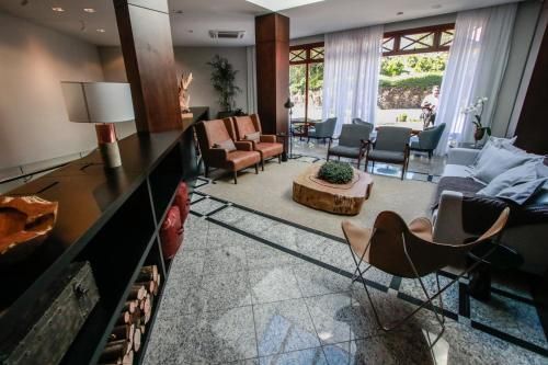 Sala de estar moderna com cadeiras, sofá e grandes janelas com vista para um pátio.
