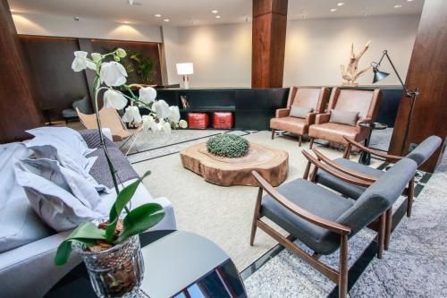 Sala de estar moderna com cadeiras cinza e bege, mesas de centro, orquídea branca e iluminação suave.