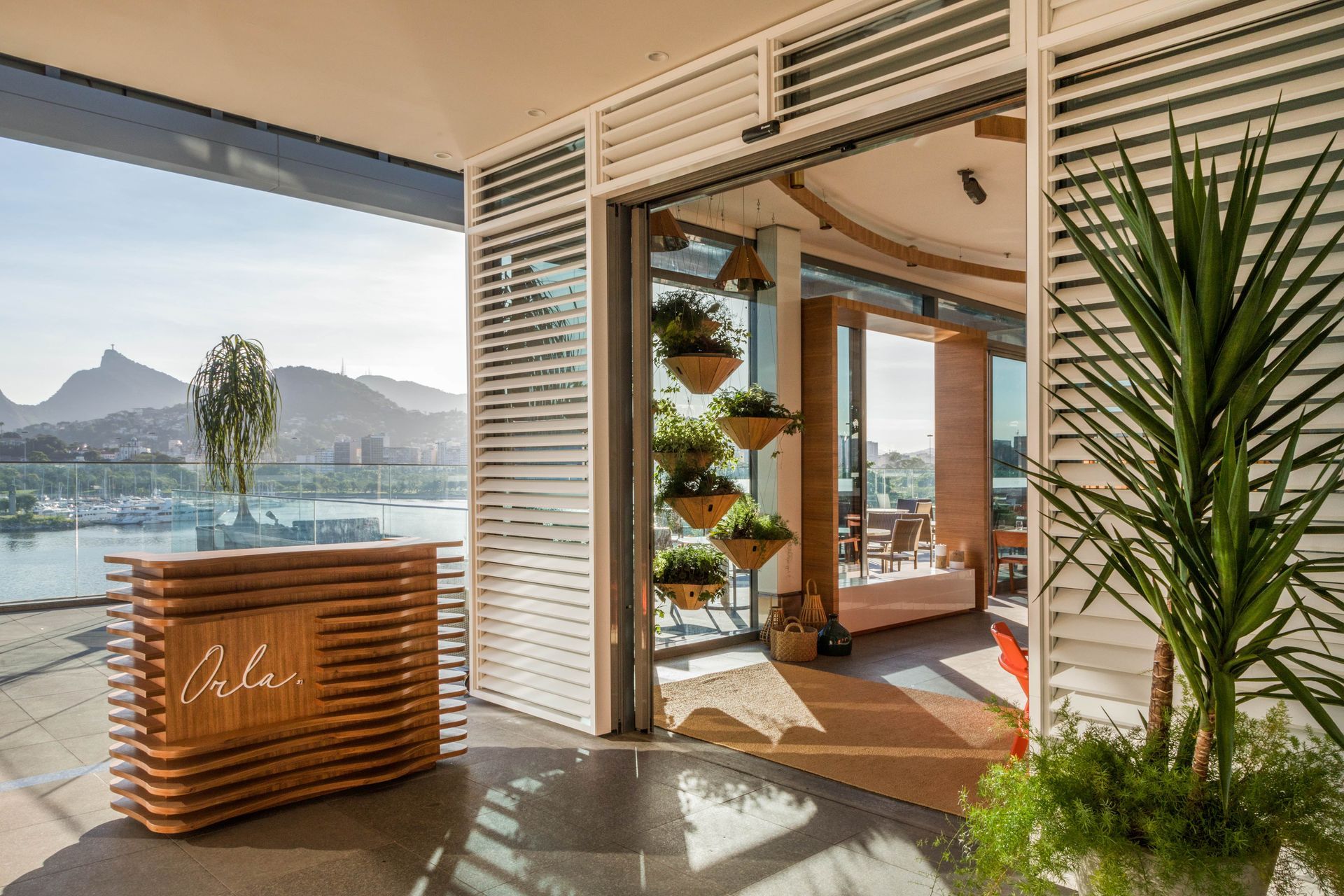 Terraço aberto com vista para o lago, bar de madeira e lounge luminoso com espaços internos e externos.