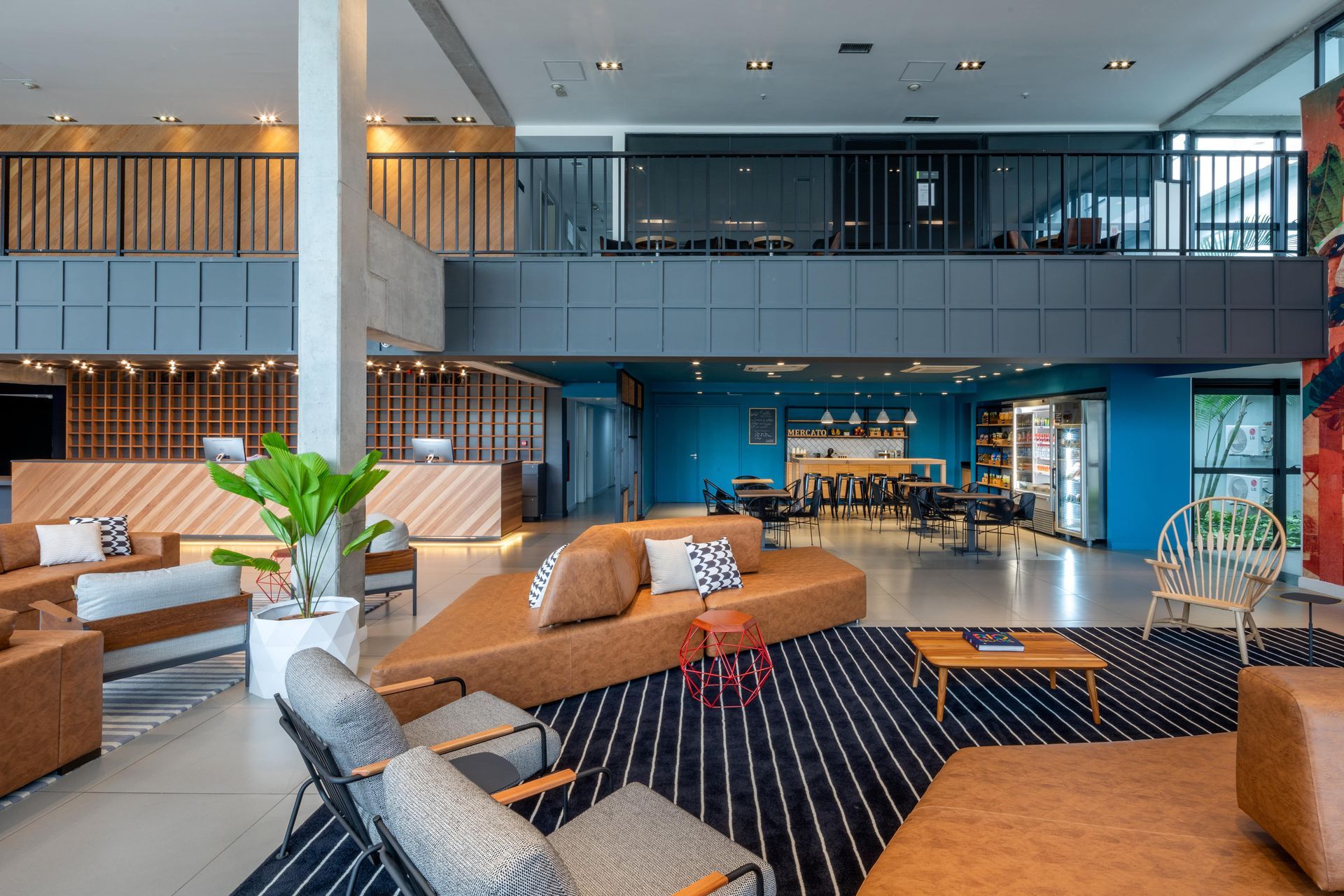 Lobby de hotel moderno com assentos em tons de bege, tapete estampado e parede de destaque em azul.
