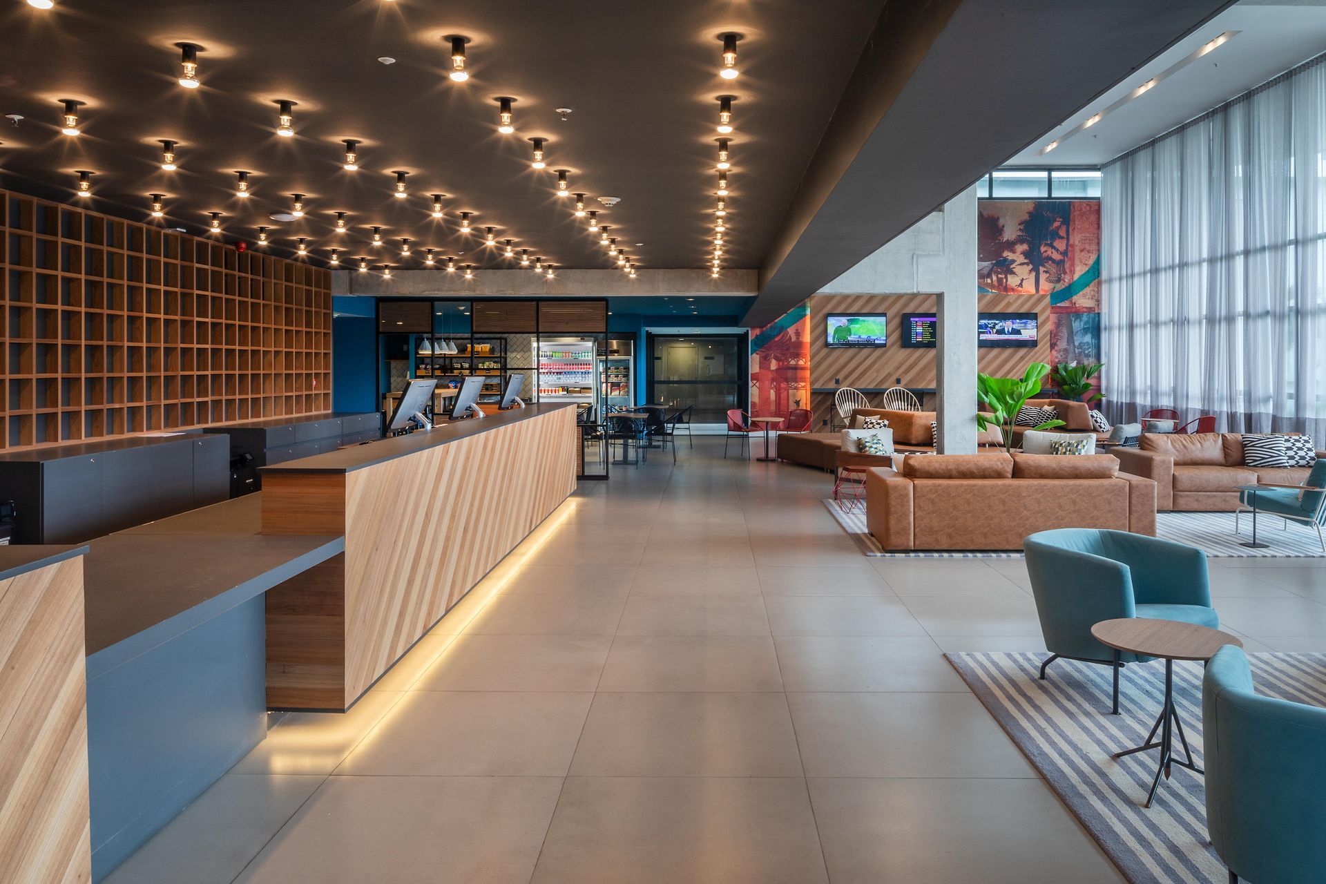 Lobby de hotel moderno com iluminação aconchegante, balcão de recepção em madeira, sofás e janelas amplas.