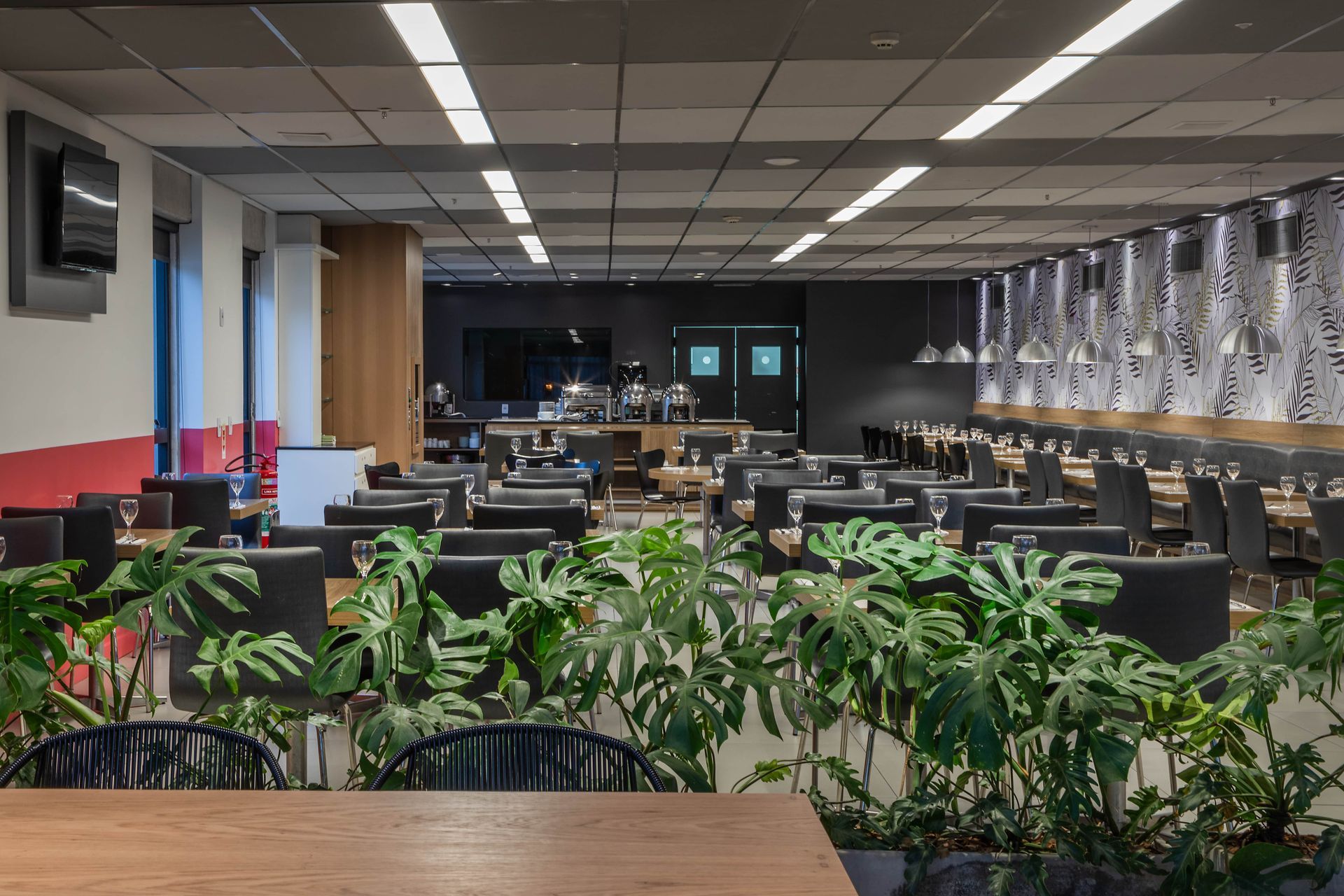 Sala de estar moderna com mesas, cadeiras, plantas e iluminação de teto em um espaço de trabalho aberto.