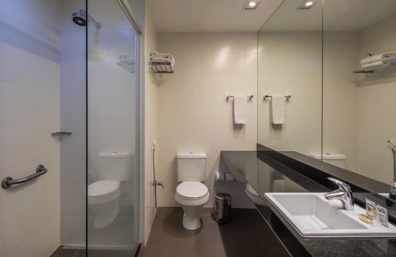 Banheiro moderno com box de vidro, vaso sanitário, pia e bancada com amplo espelho.