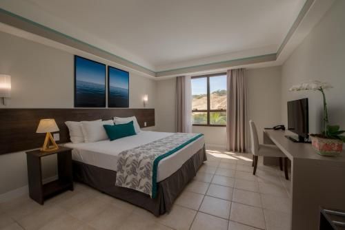 Quarto de hotel moderno com cama king-size, escrivaninha, detalhes em azul-petróleo e vista para a varanda.