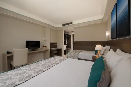 Quarto de hotel moderno com duas camas, escrivaninha, TV e paredes bege.