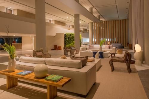 Sala de estar moderna e luxuosa de um hotel, com sofás bege, iluminação aconchegante e cadeiras de vime.