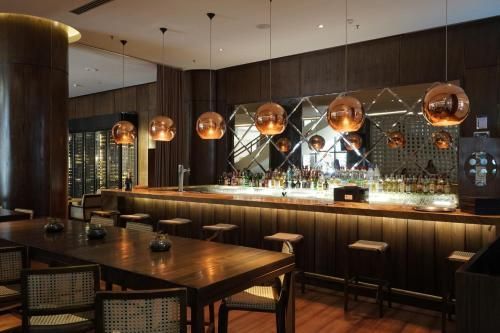 Bar moderno com iluminação suave, luminárias pendentes de cobre, mesas de madeira e um balcão comprido com banquetas.