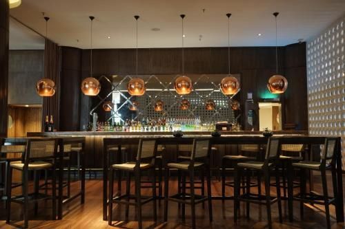 Interior de bar aconchegante e com iluminação suave, com banquetas altas, luminárias pendentes e uma parede de fundo espelhada.