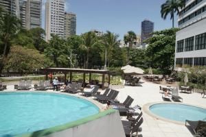 Área da piscina do resort com espreguiçadeiras, palmeiras e prédios altos ao fundo.