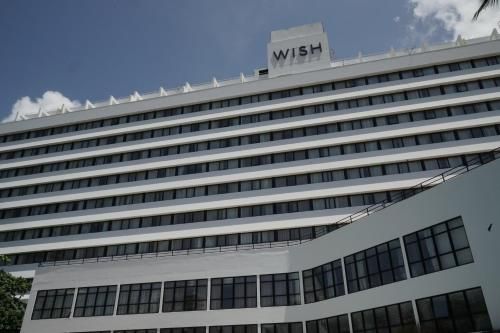 Edifício branco de vários andares do hotel WISH sob um céu parcialmente nublado.