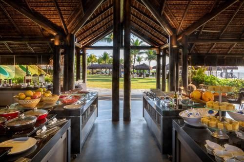 Buffet ao ar livre sob um pavilhão de palha com frutas e pratos em ambos os lados, com vista para uma piscina e jardins.