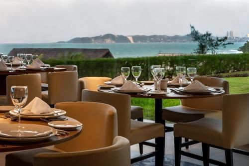 Elegante terraço de restaurante com mesas postas com vista para a praia e falésias oceânicas.