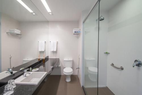 Banheiro moderno com pia dupla, vaso sanitário e box de vidro, em tons de branco e cinza.