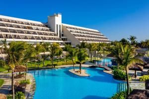 Hotel resort com uma grande piscina azul, palmeiras e céu limpo.