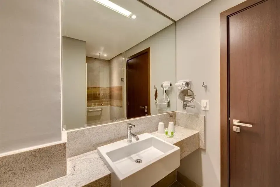Banheiro de hotel moderno com pia, espelho grande e secador de cabelo fixado na parede.
