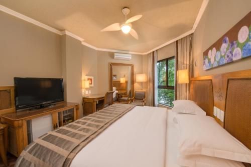Quarto com cama king-size, TV, ventilador de teto, escrivaninha e portas de vidro deslizantes para uma varanda.