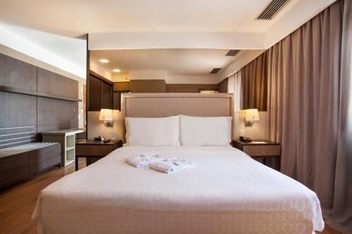 Quarto de hotel moderno com cama bem arrumada, abajures e cortinas do chão ao teto.