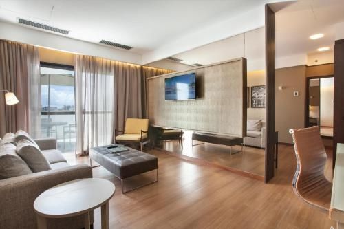Sala de estar moderna com sofá, mesa de centro, painel para TV e janelas do chão ao teto com vista para a cidade.