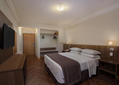 Quarto de hotel moderno com duas camas de solteiro, móveis de madeira, TV de parede e iluminação aconchegante.