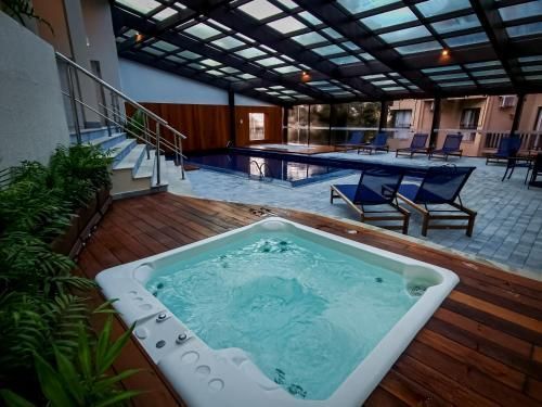 Área de piscina coberta com banheira de hidromassagem, espreguiçadeiras e deck de madeira sob teto de vidro.