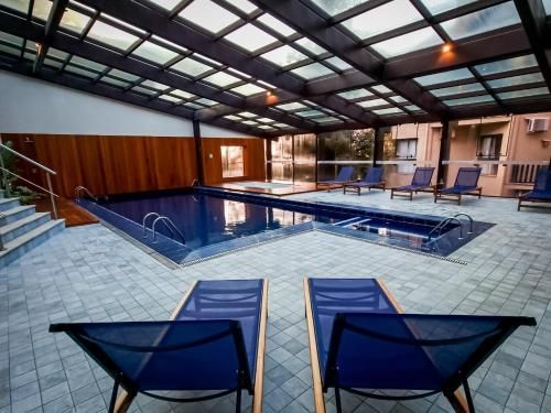 Piscina coberta com cadeiras azuis, deck de azulejos e teto coberto.