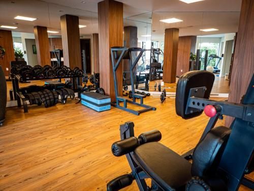 Academia moderna com piso de madeira, espelhos, bancos de musculação, halteres e aparelhos de ginástica.