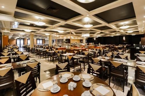 Sala de jantar espaçosa do restaurante com mesas bem arrumadas, cadeiras pretas e iluminação aconchegante no teto.