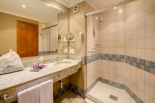 Banheiro com pia, espelho, toalha e box de chuveiro com azulejos bege e faixa decorativa azul.