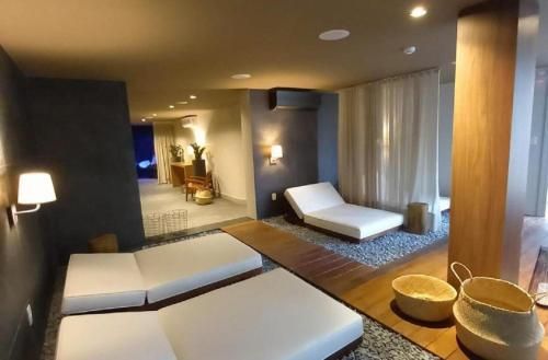 Sala de spa moderna com espreguiçadeiras baixas brancas, iluminação aconchegante, cortinas e cestos de vime.