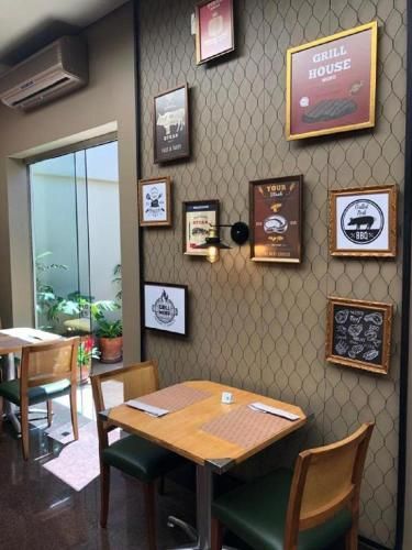 Cantinho aconchegante de café com mesa e cadeiras de madeira, obras de arte emolduradas na parede e uma porta que dá para um jardim interno iluminado.