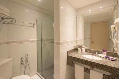 Banheiro moderno com box de vidro, bancada de granito, espelho e paredes revestidas com azulejos brancos.