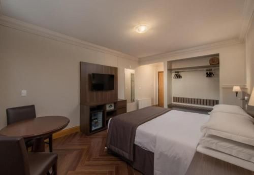 Quarto de hotel pequeno com cama, TV, mesa redonda e armário aberto.