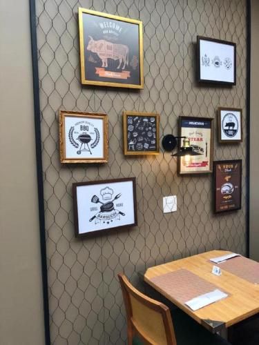 Quadro decorativo acima de uma mesa de madeira em um canto pouco iluminado de um café, com papel de parede estampado.