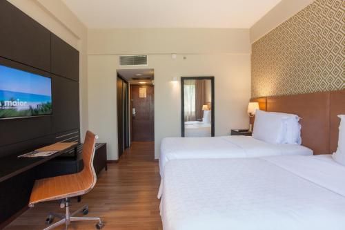 Quarto de hotel moderno com duas camas de solteiro, escrivaninha, TV e piso de madeira aconchegante.