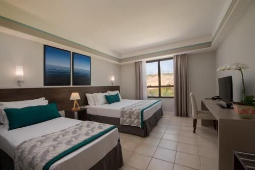 Quarto de hotel moderno com duas camas, TV, mesa de trabalho e varanda com vista.