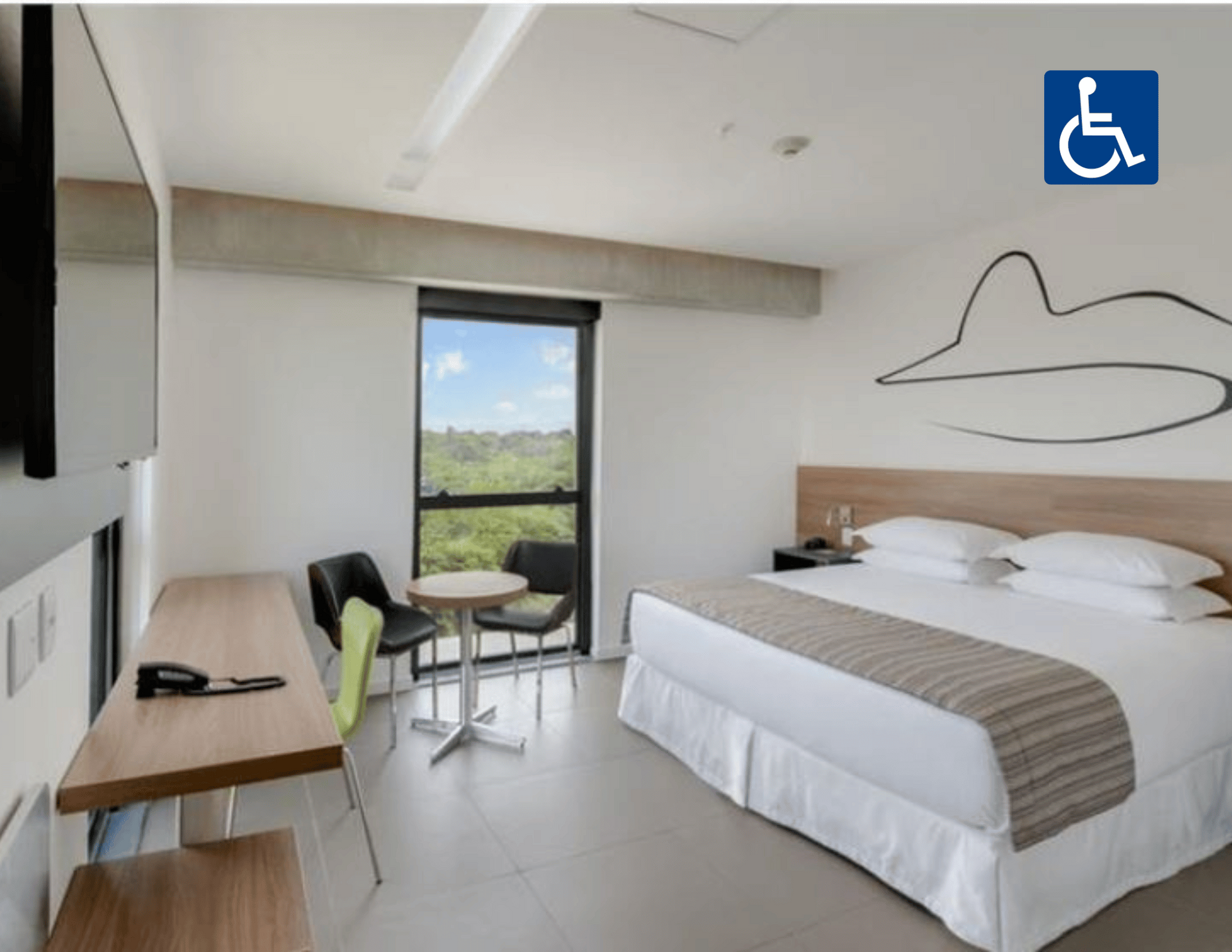 Quarto de hotel acessível com duas camas, escrivaninha e varanda com vista para a vegetação e as montanhas.