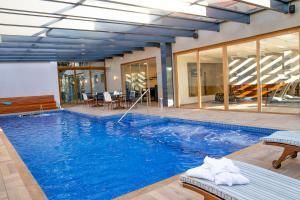 Piscina interior com água azul, espreguiçadeiras e portas de vidro num ambiente de spa moderno.
