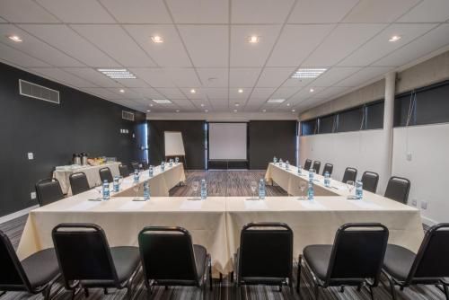 Sala de conferências vazia com mesa em formato de U, cadeiras pretas e tela de projeção ao fundo.
