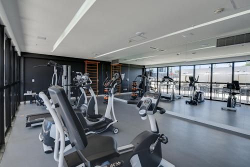 Interior de academia moderna com fileiras de bicicletas ergométricas, aparelhos de cardio e grandes janelas com vista para a cidade.