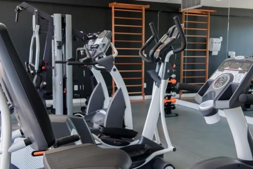 Academia moderna com aparelhos de ginástica, bicicletas ergométricas e barras de escalada de madeira fixadas na parede.