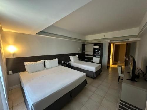 Quarto de hotel com duas camas, iluminação aconchegante e uma TV sobre a cômoda.